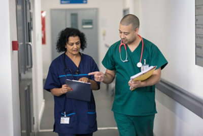 A man and a woman in scrubs holding a folder and clipboard, respectively.