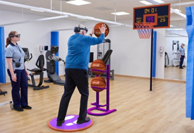 A basketball court with a basketball hoop, a digital scoreboard, and a rack of basketballs.