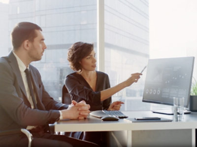 Eine Frau zeigt auf einen Computerbildschirm, während sie neben einem Mann sitzt.