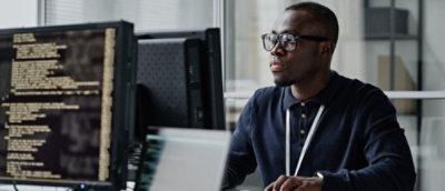 A man wearing glasses and a blue shirt sitting at a desk with a computer.