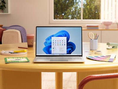 Laptop z kolorowym ekranem głównym stojący na okrągłym drewnianym stole z różnymi artykułami biurowymi.