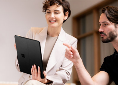 Two individuals in a business setting, one holding a tablet and the other gesturing with their hand.