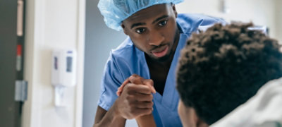 Two doctors and a man in a suit stand together in conversation, reviewing documents.
