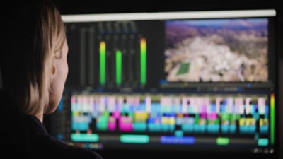 Person working on video editing software with colorful timelines and audio levels visible on the monitor.