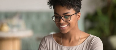 A person with short curly hair and glasses smiles while looking down.
