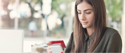 A woman is sitting indoors, holding a smartphone in one hand and a credit card in the other