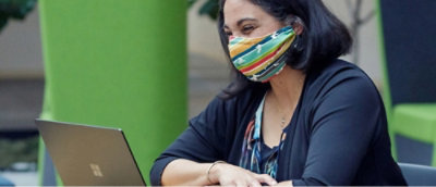 A woman wearing a colorful face mask works on a laptop.
