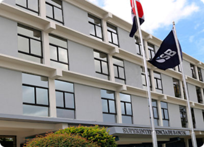 Un edificio de oficinas de cuatro plantas con el signo "Superintendencia de Bancos", varias ventanas