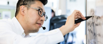 Man met headset die op een whiteboard schrijft in een kantooromgeving.