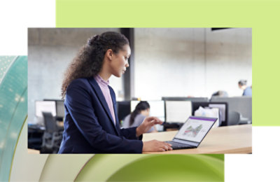 A woman with curly hair working on a laptop in a modern office environment.