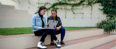 Two women sitting on steps looking at a laptop.