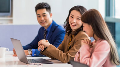 Grupa ludzi siedzi przy stole i patrzy na laptopa.