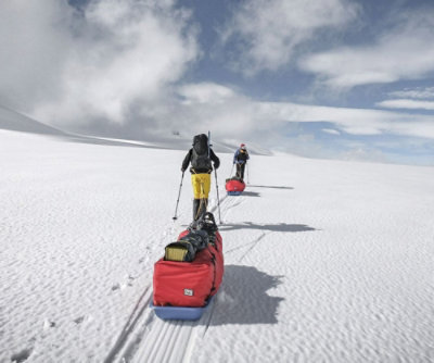 Grupa ludzi ciągnie sanki po śniegu.