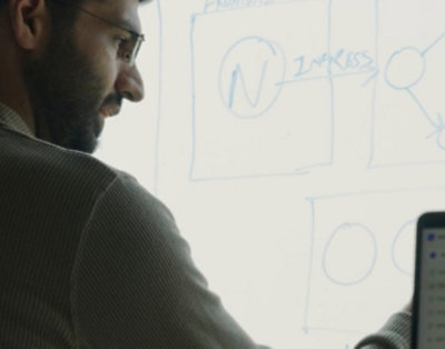 A man with glasses and a beard looks at a whiteboard with blue writing.