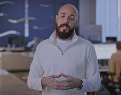 A close-up of a man's face with a beard and a white jacket visible.