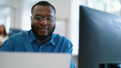 A man wearing glasses looking at the laptop and smiling
