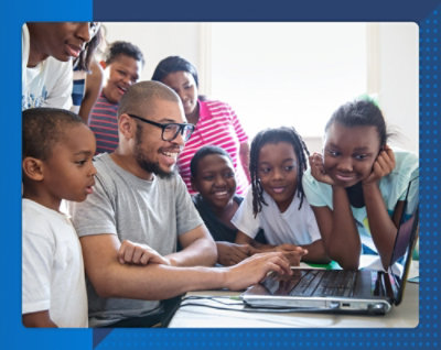 Un groupe hétéroclite d’enfants souriants et un adulte se rassemblent autour d’un ordinateur portable, partageant un moment d’apprentissage joyeux qui transmet un sentiment de communauté studieuse.