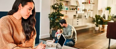 A woman sitting on the floor with a laptop and a man in the background.