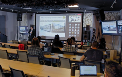 A person presenting gate design concepts on a large screen to a classroom of students