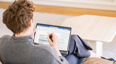 A person sitting on a couch using a pen and tablet to edit a Word document