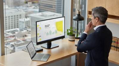 A person standing over their desk and looking at a PowerPoint presentation being displayed on a desktop monitor