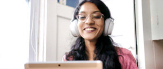 Eine lächelnde Frau mit Brille und Kopfhörern, die ihren Laptop verwendet