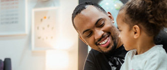 Eine lächelnde Person blickt ein Kind vor einem Laptop an, der auf dem Tisch steht.