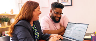 A man and woman laughing while looking at a laptop.