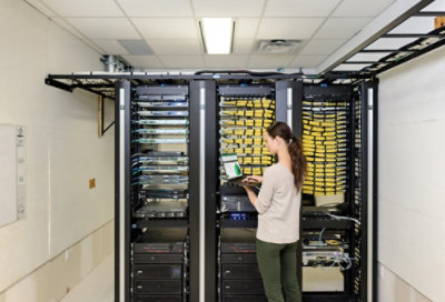 Osoba, která stojí před blade servery a používá tablet.