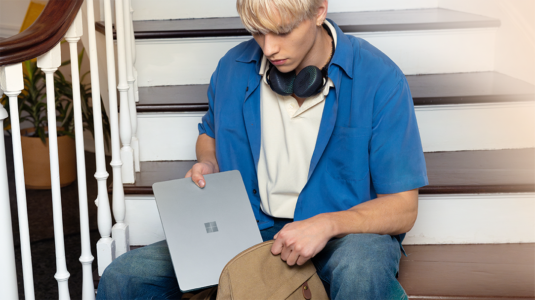 An image of a young man placing a Surface Laptop into his backpack