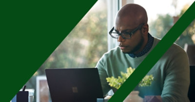 En mand, der arbejder foran en bærbar computer, mens han sidder på et skrivebord. 