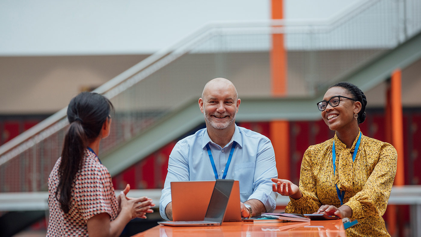 Three teachers sitting at a table, having a discussion in the lobby area of their school