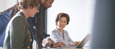 Drei Personen im Gespräch in einem Büroraum Eine Person nutzt einen Laptop, während die anderen zuschauen.