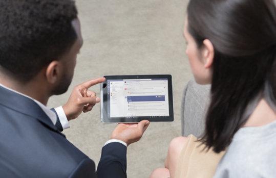 Dva lidé, kteří se dívají na zprávy Teams na tabletu.