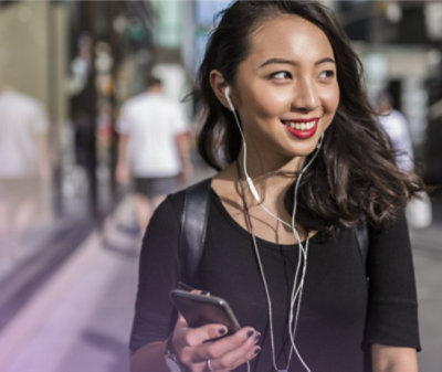 Personne souriant et portant des écouteurs. Elle marche dans une rue avec un téléphone mobile dans ses mains 